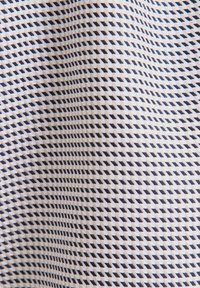 Primo piano di un tessuto con un motivo geometrico a diamante bianco e nero che crea un effetto texturizzato e ondulato.