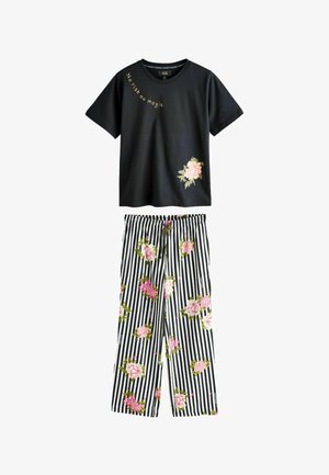 Schwarzes Kurzarmhemd mit dem Schriftzug "No risk no magic" und rosa Blume, kombiniert mit schwarz-weiß gestreiften Hosen mit rosa Blumenmuster.