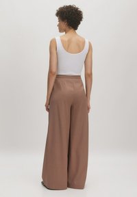 Braune, weit geschnittene Hose mit hoher Taille, die eine glatte Textur und subtile Falten aufweist. Kombiniert mit einem weißen ärmellosen Top.