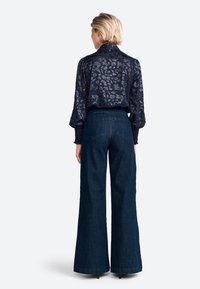 Navy patterned blouse with long sleeves, high neckline, and textured fabric, paired with dark wide-leg jeans featuring a classic cut.