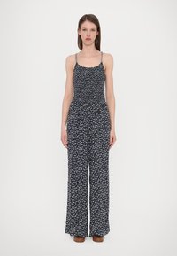 Tuta nera con piccolo motivo floreale blu, spalline sottili, busto arricciato e pantaloni a gamba larga. Tessuto morbido con vestibilità comoda.