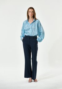 Light blue floral button-up shirt with loose sleeves, paired with dark navy tailored pants and strappy sandals. Simple, modern design.