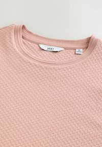Lyserød tekstureret sweater med runder halsudskæring, der har ribbede kanter og et mærkat med "NEXT" og størrelse "M."
