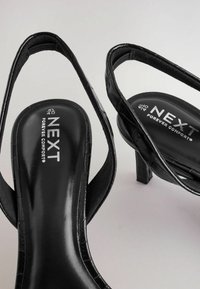 Schwarze Absatzsandalen mit einem eleganten Design, Krokodil-Textur, offener Zehenpartie und markierten Innensohlen. Der Absatz ist kurz und blockförmig.
