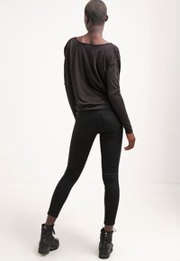 Černý dlouhý rukáv top s volným střihem a nařasenými detaily na rameni, doplněný úzkými černými legínami a černými šněrovacími botami.