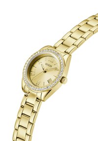Montre-bracelet dorée avec un cadran rond, des chiffres romains, une lunette en cristal et un bracelet à maillons en métal poli.