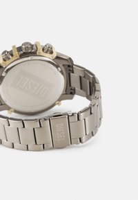 Orologio cronografo in metallo con cinturino in acciaio inox argento, push-button accentati in oro e fondo tondo con il logo "DIESEL" inciso.