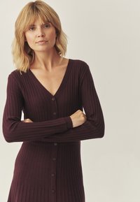 Tumšs burgundijas garām piedurknēm, dziļa V veida kakla izgriezuma kardigans ar ribotu tekstūru un pilnu pogu aizdari. Mīksts, pieguļošs dizains.