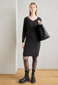 Czarna szara dzianinowa sukienka ribbed z dekoltem w kształcie V, długimi rękawami i dopasowanym krojem. Połączona z czarnymi botkami za kostkę i teksturowaną czarną torbą typu tote.