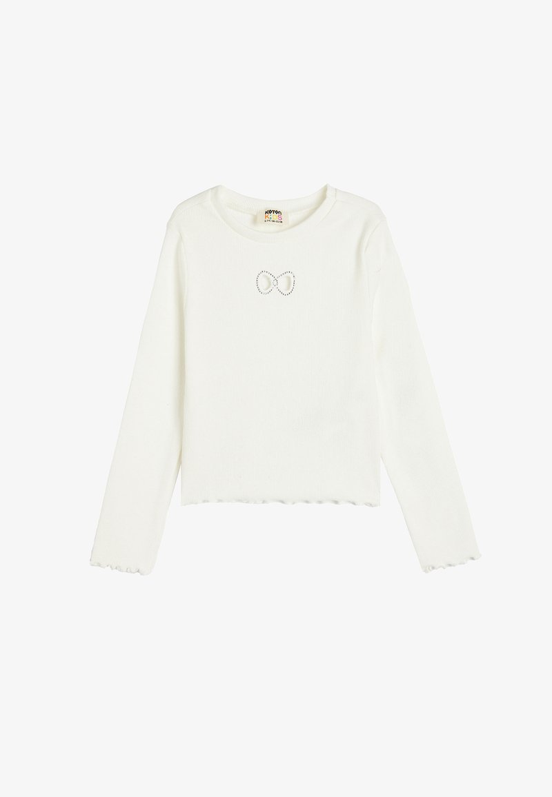 White long-sleeve shirt made of ribbed fabric, featuring a scalloped hem and a small, decorative bow detail at the chest.
