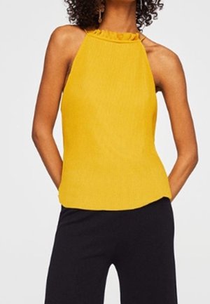 Żółty top na ramiączkach z teksturowanym, prążkowanym wzorem. Posiada marszczony dekolt i luźny krój, w zestawieniu z czarnymi spodniami.