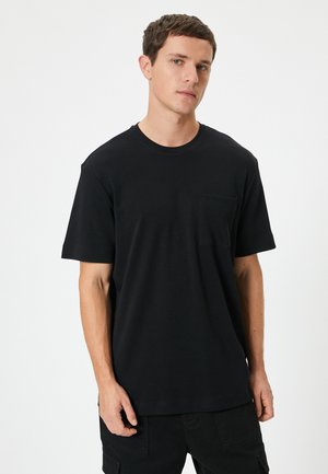 Camiseta negra de manga corta con un corte relajado, que presenta un bolsillo en el pecho, cuello redondo y tejido de algodón suave.