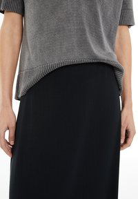 Suéter gris de punto con mangas cortas, con un ribete en la parte inferior, combinado con una falda negra que tiene rayas verticales y una textura suave.