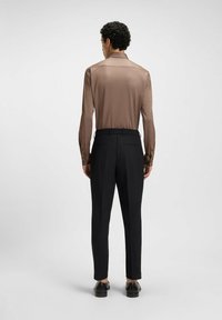 Bruine, gladde, langdfracige shirt gecombineerd met zwarte, op maat gemaakte broek, met een elastische tailleband en elegante schoenen.