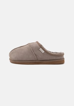 Zapatilla de estar por casa de ante marrón claro con forro interior peludo, suela de goma y una pequeña etiqueta de tela en el lateral con la palabra "Shepherd."