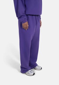 Lilla joggebukser laget av mykt stoff, med elastisk midjebånd og lommer. Kombinert med joggesko med reflekterende detaljer.