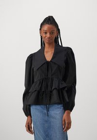 Svart bluse med puff-lagede ermer og stor krage, snøring i midjen, lagdelte volanger og glatt stoff, kombinert med et denimskjørt.