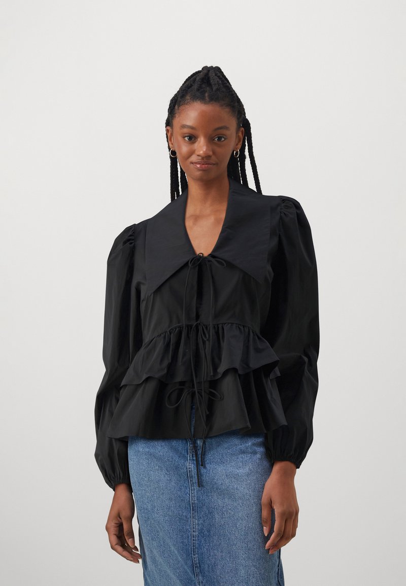 Svart bluse med puff-lagede ermer og stor krage, snøring i midjen, lagdelte volanger og glatt stoff, kombinert med et denimskjørt.