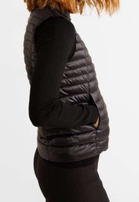 Schwarze Steppweste mit schlankem Schnitt, gestepptem Muster, hohem Kragen und Seitentaschen, getragen über einem langärmeligen schwarzen Oberteil.