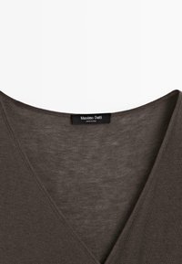 Gros plan d'un vêtement marron à col en V avec une étiquette noire Massimo Dutti cousue à l'intérieur de l'encolure.