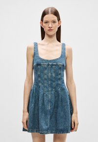 Τζιν φόρ�εμα με τετράγωνη λαιμόκοψη και φαρδιές τιράντες. Εφαρμοστός κορσές με λεπτομέρειες από πιντάκια, φουσκωτή φούστα και ακατέργαστο στρίφωμα. Μπλε χρώμα.