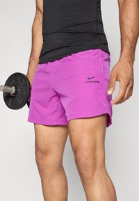 Bright pink Nike Pro shorts with a black logo, featuring a lightweight design and side slits for mobility. Adjustable waistband for comfort.