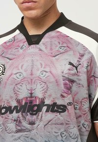 Grafisches T-Shirt mit einem Design eines rosa Tigerface, schwarzem Puma-Logo, strukturiertem Stoff und einem V-Ausschnitt mit kontrastierenden schwarzen und weißen Ärmeln.