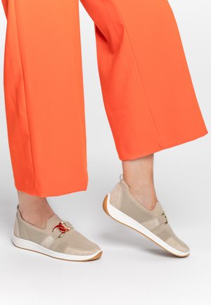 Beige knit slip-on shoes with suede accents, featuring a decorative red and gold hardware detail, and a white rubber sole.