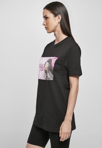 Schwarzes Baumwoll-T-Shirt mit Rundhalsausschnitt, das ein farbenfrohes grafisches Design eines Charakters vor einem pinken Burst-Hintergrund zeigt.