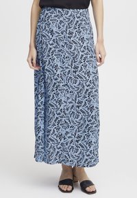 Maxi-jurk in lichtblauw met een zwart bladdessin. Vloeiende stof, hoge taille en zijsplit. Gecombineerd met zwarte hakken.