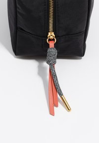 Bolso de lona negro con cremallera dorada y un tirador de borla en coral y gris, complementado con un detalle dorado en el extremo de la borla.