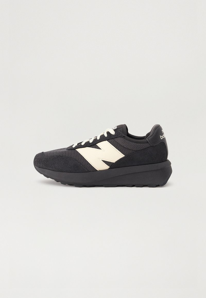 Baskets de sport noires avec un logo "N" blanc, des lacets blancs et une semelle noire épaisse, vues de profil sur un fond uni.