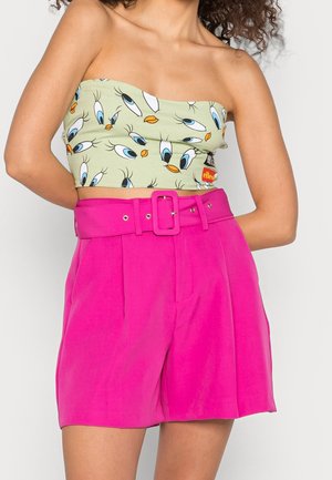 Licgroene strapless crop top met patroon van blauwe ogen en oranje snavels, gecombineerd met felroze, hoog getailleerde short met ceintuur.