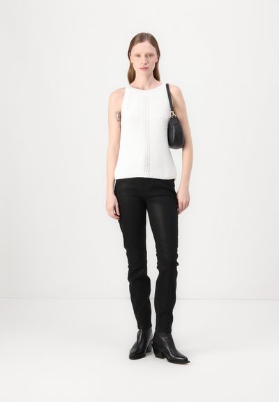 Haut sans manches en tricot blanc avec un motif texturé associé à un pantalon noir ajusté et des bottes noires à talons, le tout complété par un petit sac à main noir.
