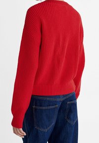 Roter gestrickter Pullover mit einem strukturierten Muster, breiten gerippten Bündchen und Saum. Getragen mit dunkelblauen Jeans. Rückansicht gezeigt.