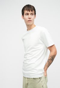 Λευκό βαμβακερό t-shirt με στρογγυλή λαιμόκοψη, κοντά μανίκια και χαλαρή εφαρμογή, σε σ�υνδυασμό με ανοιχτό πράσινο τζιν παντελόνι με ξεθωριασμένη υφή.