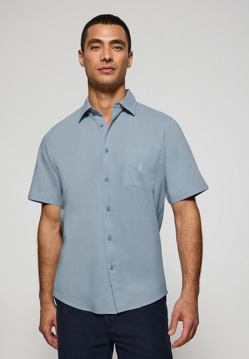 Camicia a maniche corte di colore azzurro chiaro, realizzata in tessuto morbido, con chiusura a bottoni sul davanti, colletto piatto e taschino sul petto con un delicato dettaglio del logo.