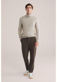 Pulover cu guler înalt de culoare gri deschis, ajustat. Pantaloni tapered de culoare maro închis, cu textură netedă. Adidași albi cu accente verde deschis și tălpi din gumă.
