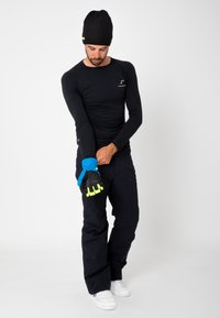 Långärmad svart termotröja, mörka byxor och klibbiga blå handskar med texturerad svart palm och neonlysande detaljer. Modellen justerar handskarna på höger hand.