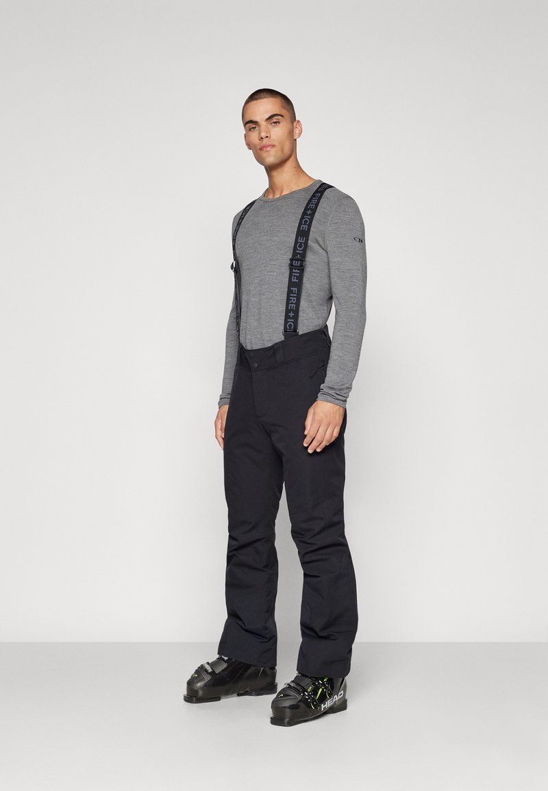 Μαύρα παντελόνια σκι με ρυθμιζόμενους ιμάντες, σε συνδυασμό με μακρυμάνικο γκρι μπλουζάκι. Διαθέτει κομψό σχεδιασμό και είναι εξοπλισμένο για χειμερινά σπορ.