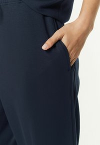 Navyblaue Jogginghosen aus weichem Material mit einer Seitentasche. Das Design zeichnet sich durch eine glatte Oberfläche und eine schlanke Form aus.