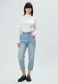 Weißes Langarm-Turtleneck-Shirt kombiniert mit hellblauen High-Waist-Jeans, aufgerollten Säumen und schwarzen Slippern mit goldener Kettenakzentuierung.