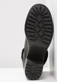 Suela de bota de cuero negro con una superficie texturizada y con relieve, que presenta un patrón distintivo y un tacón curvado. Marcas claras de la marca y el tamaño presentes.