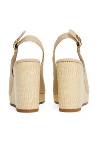 Beige kilehæle sandaler med et tekstureret stofoverdel, lukket bagpå og spænde lukning. Platformen har et vævet design med en solid bund.