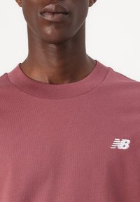 Bordeauxfarbener Rundhalsausschnitt-Sweatshirt mit geripptem Halsausschnitt und weißem, gesticktem "N"-Logo auf der Brust. Glatte Baumwolltextur, minimalistisches Design.