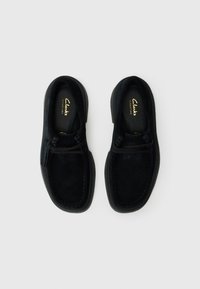 Sorte semskede slip-on sko med rund tå, kontrasterende søm og en fleksibel gummisål. Har minimalt med hardware og merking.