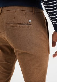 Brązowe spodnie w jodełkę z tylną kieszenią ozdobioną srebrnym guzikiem, wykonane z teksturowanej tkaniny o dopasowanym kroju.