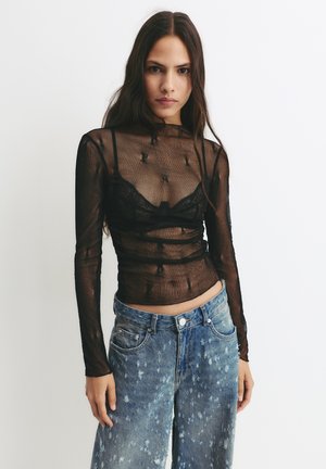 Sort gennemsigtig langærmet top med struktureret mesh og lagdelt design. Kombineret med slidte lyse denimjeans med malerpletter.