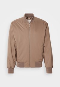 Blouson aviateur marron clair avec fermeture éclair devant, col, poignets et ourlet côtelés, et poches latérales zippées sur un fond uni.