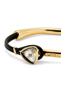 Bracelet doré avec une pierre précieuse claire en forme de triangle, associé à un bracelet en cuir noir et une finition lisse et polie.
